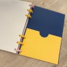 Bolsillo amarillo vacío junto a una hoja de rayas de la agenda 2026-27 con sistema de discos, diseño Plumas