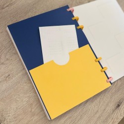 Bolsillo para notas amarillo y azul visto desde la contraportada de la agenda 2026-27, diseño Plumas